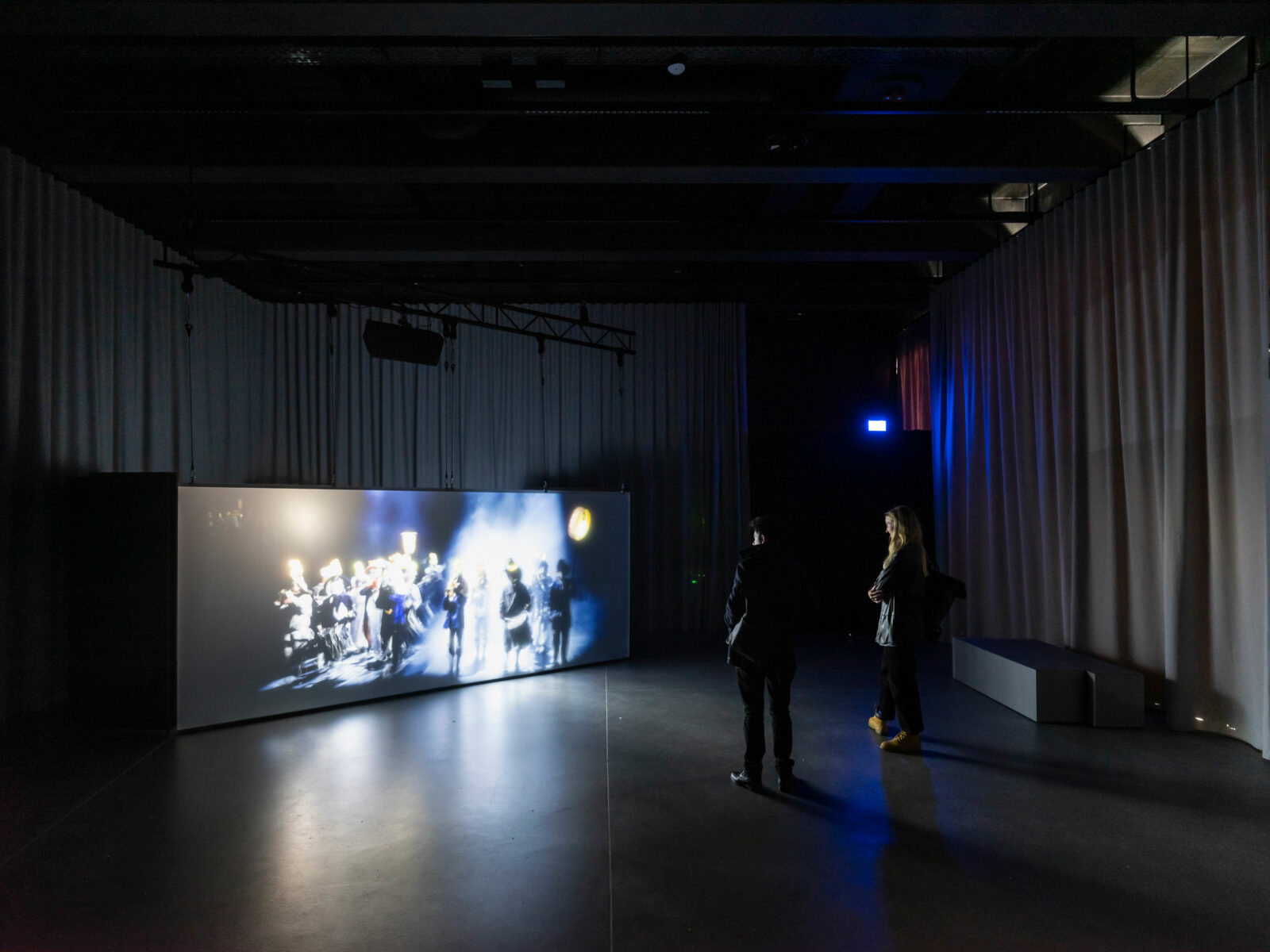In einem abgedunkelten Raum stehen Besucher, die die Filme von Clément Cogitore auf riesigen Displays anschauen.