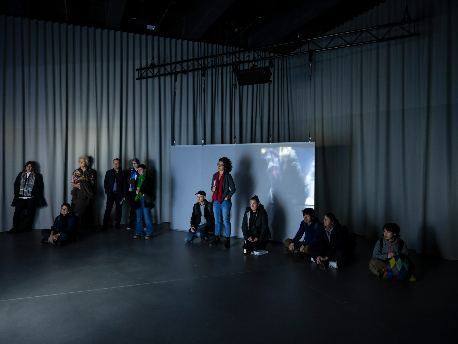 Visitors stand in a darkened room watching Clément Cogitore's films on huge displays.