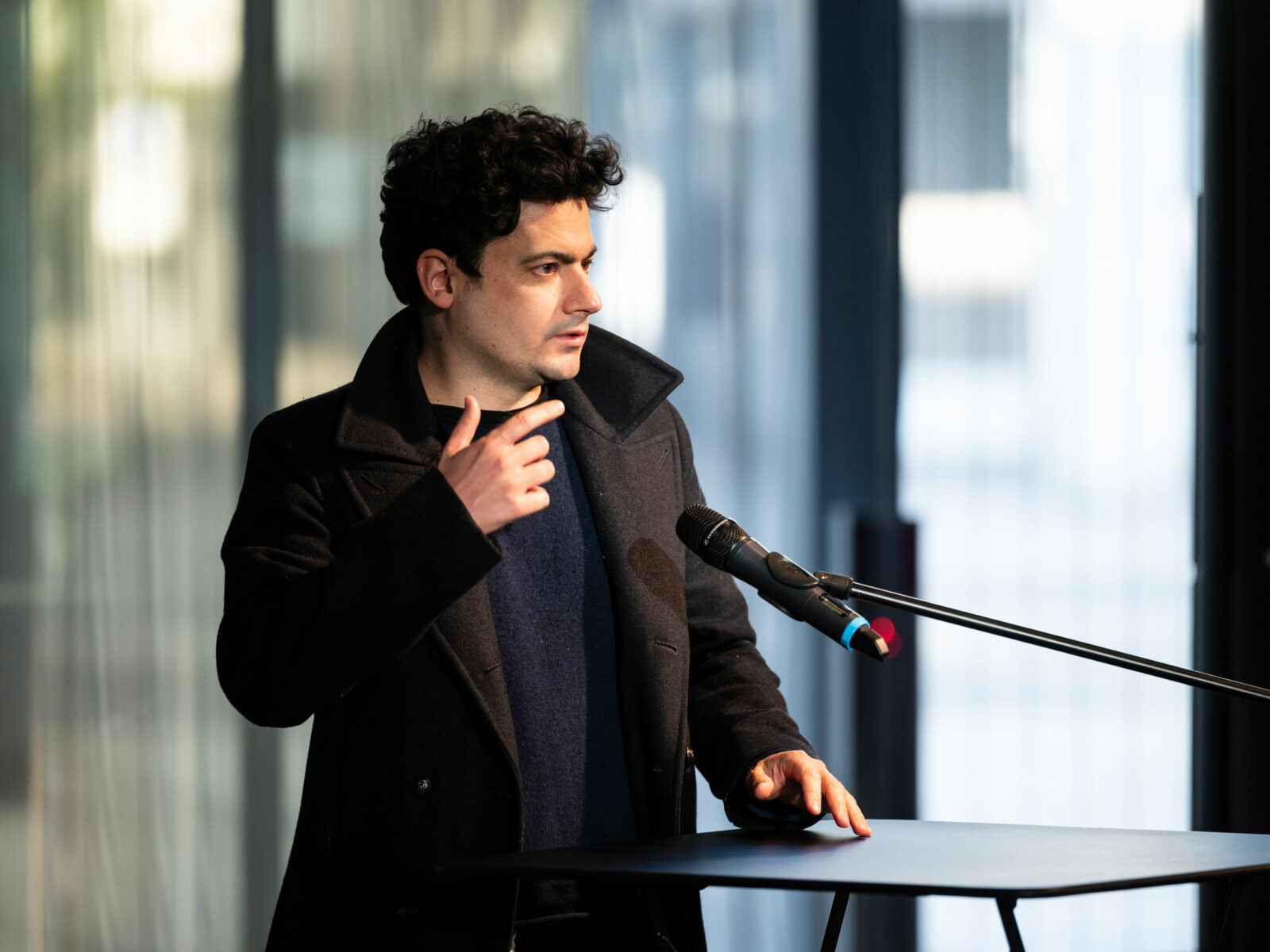 Clément Cogitore stands at a lectern and speaks with a sweeping gesture.