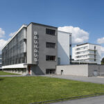 Blick auf die Südfassade des historischen Bauhausgebäudes mit dem großen, vertikalen Bauhaus-Schriftzug, bei Sonnenschein und blauem Himmel.