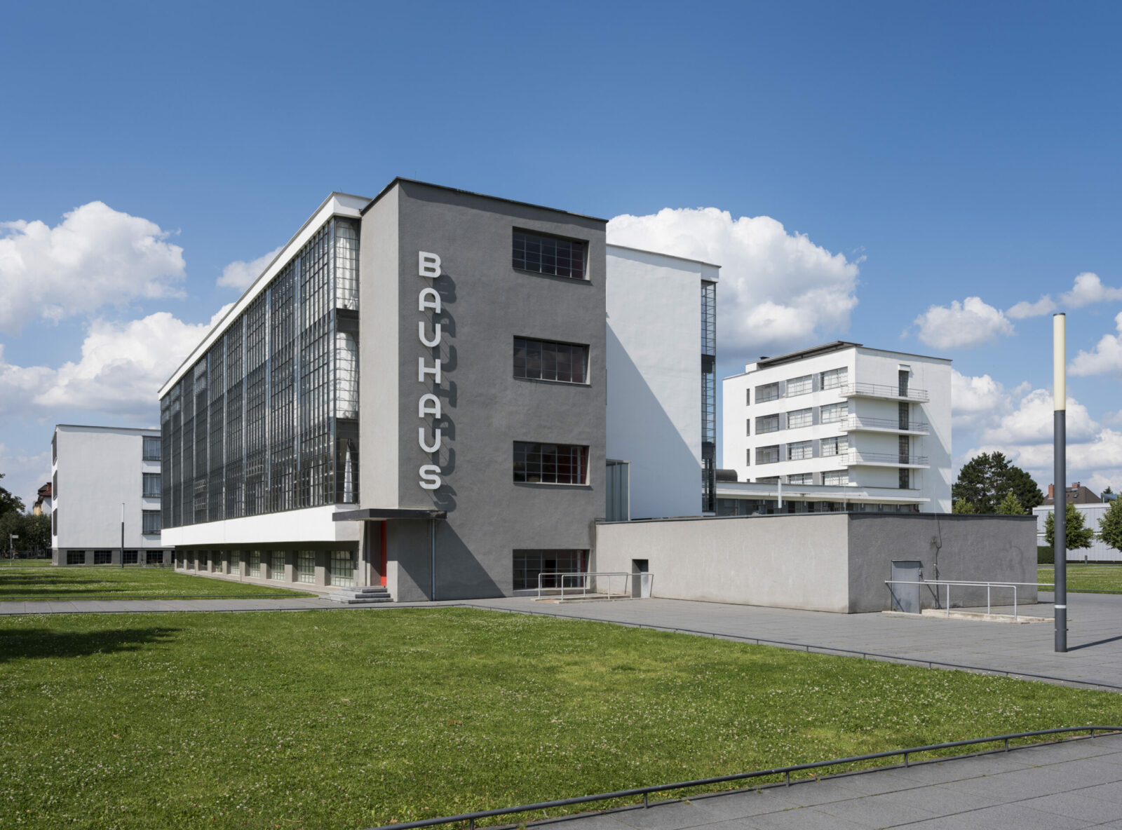 Blick auf die Südfassade des historischen Bauhausgebäudes mit dem großen, vertikalen Bauhaus-Schriftzug, bei Sonnenschein und blauem Himmel.