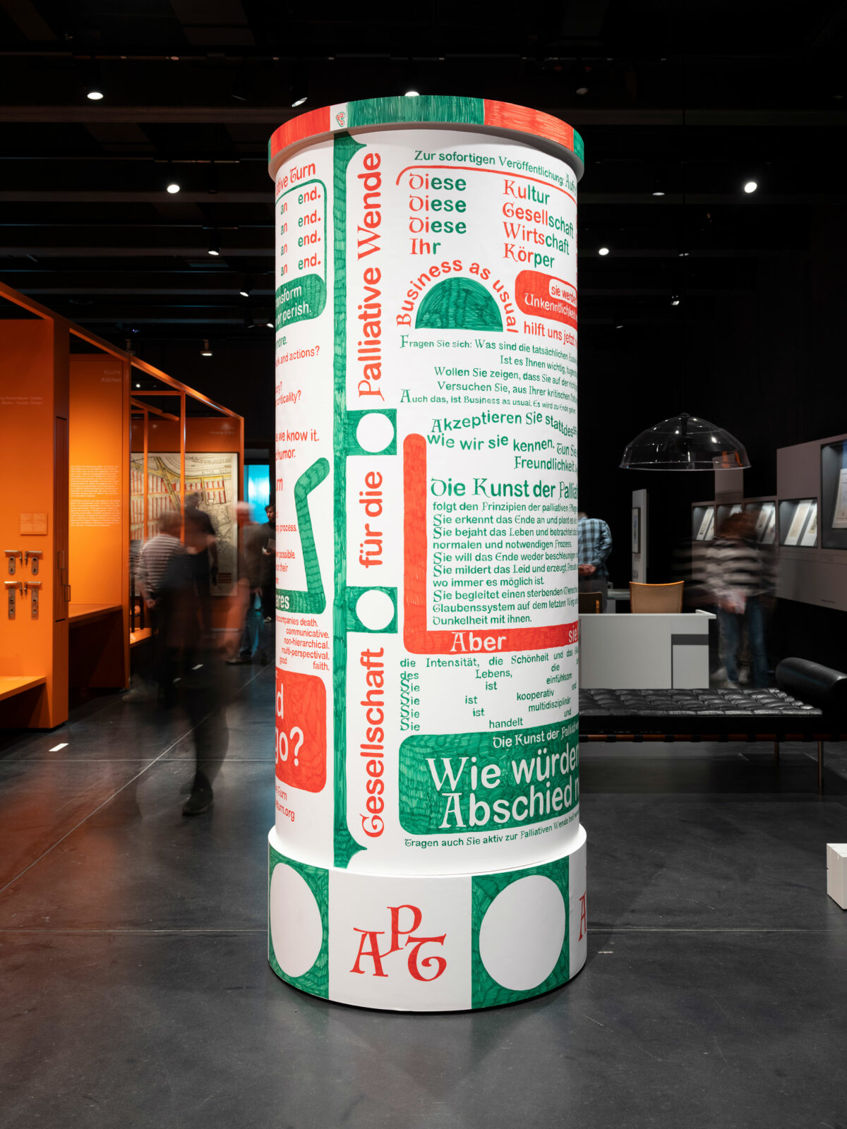 Eine original große Litfasssäule steht mitten im Ausstellungsbereich. Sie ist mit grüner und Roter Schrift von unten bis oben mit kleinen und großen Botshcaften des APT beschriftet.