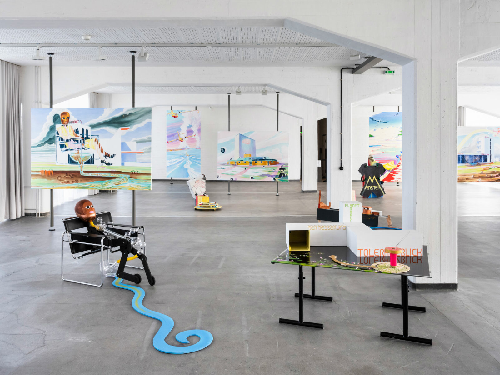 View of the large, bright workshop room in the Bauhaus building. Large pictures are mounted on supports in the room. There are a few models on the floor.