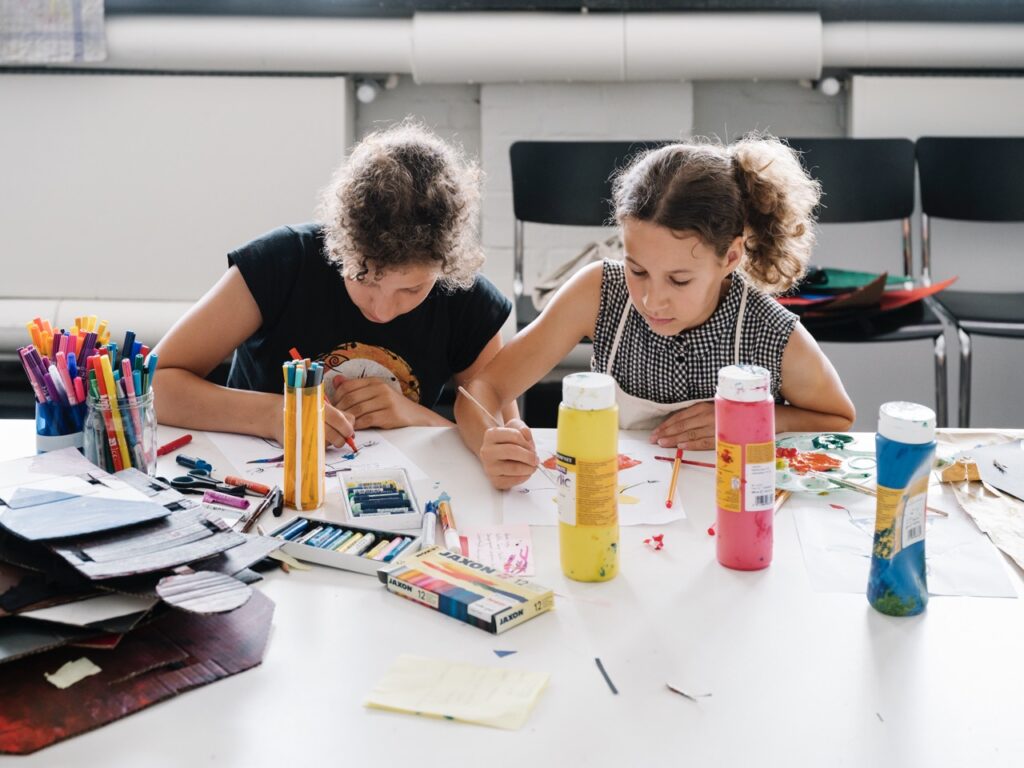 Zwei Kinder sitzen an einem Tisch und gestalten mit Stiften und Farben.