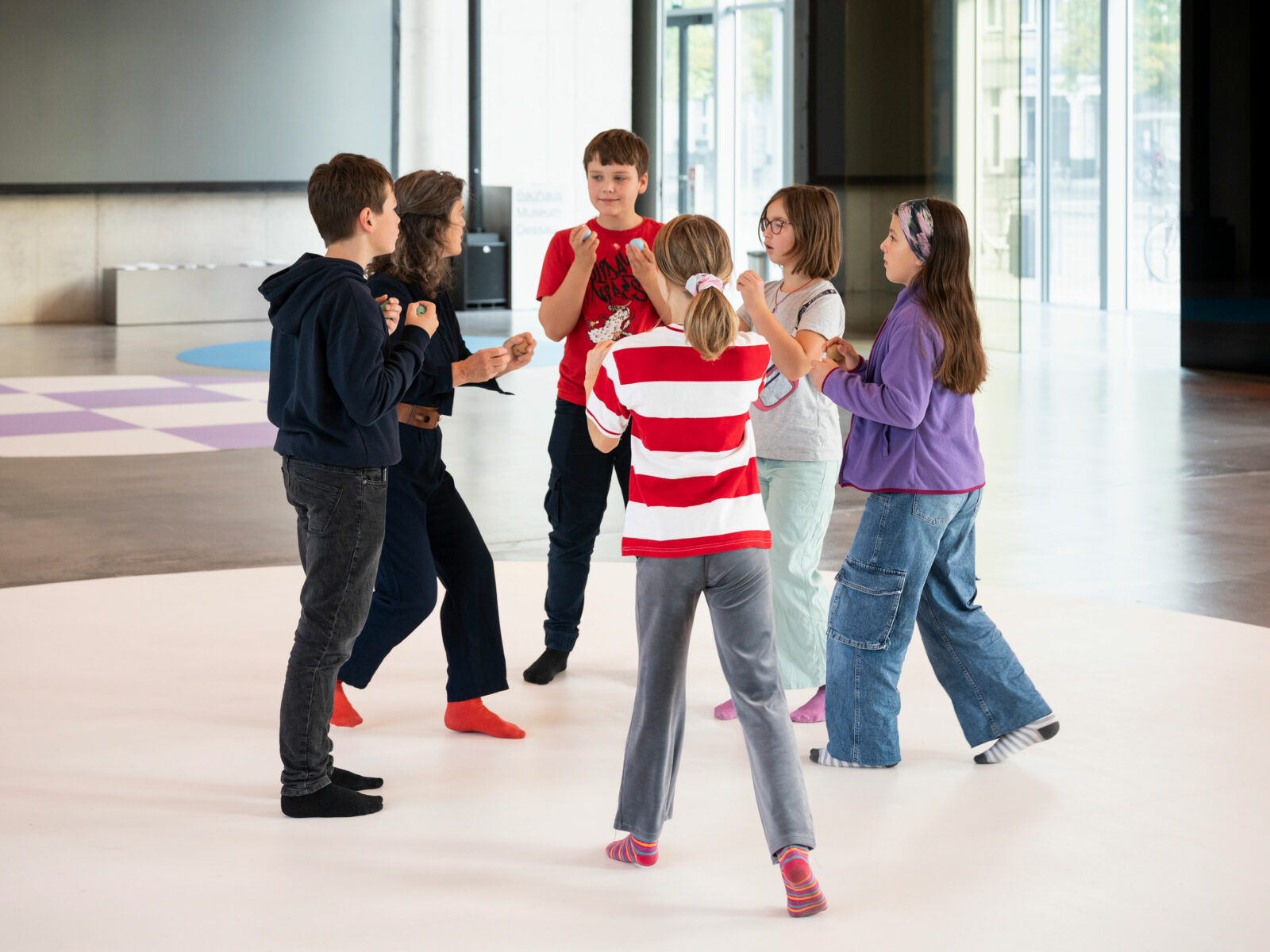 Five children run towards each other in a circle. They hold small balls in front of their bodies.