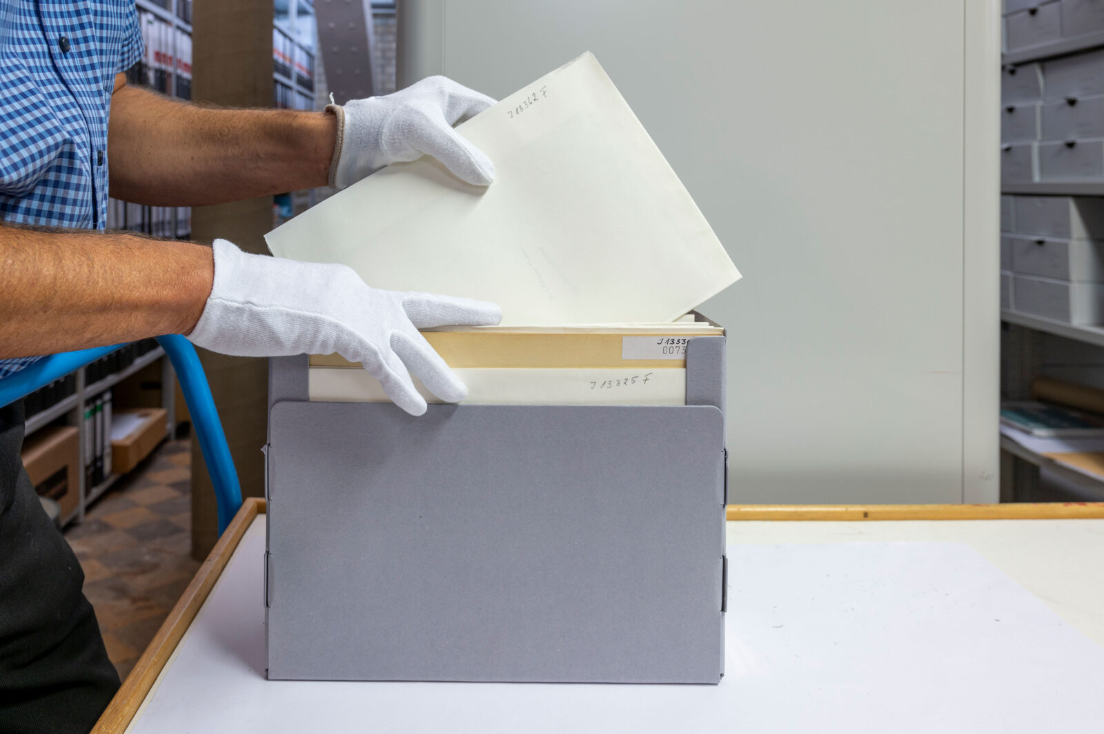 Ein Mitarbeitender des Archivs trägt weiße Handschuhe und zieht einen Umschalg aus einem Dokumentenkaroton.